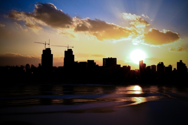 Silhueta da cidade pelo mar contra o céu durante o pôr do sol