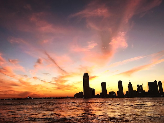 Foto silhueta da cidade pelo mar contra o céu durante o pôr-do-sol