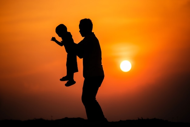 Foto silhueta da família que o pai brinca com o menino alegremente com o pôr do sol no céu