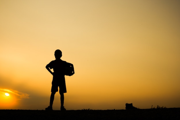 Silhueta da silhueta da aptidão Um menino que prende a esfera do futebol após o jogo, conceito do wellness do exercício.