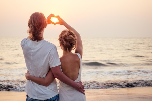 Silhueta de amantes românticos abraçados com oceano marinho com pôr do sol com símbolo de coração vermelho - conceito do Dia de São Valentim,