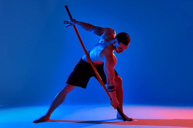 Silhueta de atleta masculino com bastão de treinamento de caratê usando ferramenta esportiva em estúdio em fundo colorido de luzes