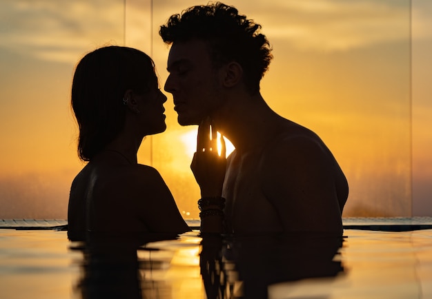 Silhueta de casal apaixonado na água do pólo infinito durante o pôr do sol. Romance e relacionamento