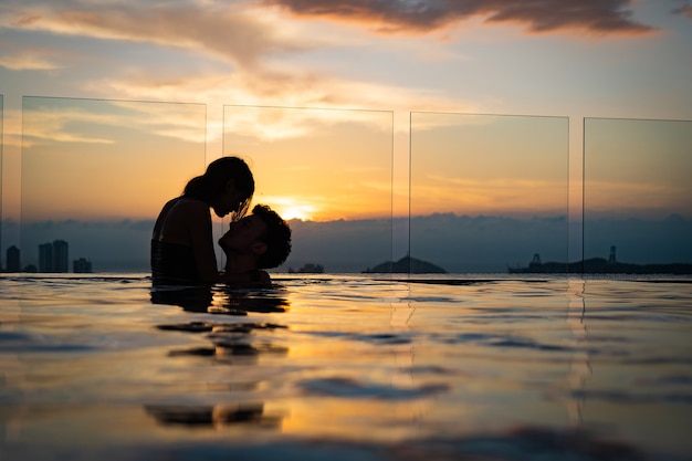 Silhueta de casal apaixonado na água do pólo infinito durante o pôr do sol. União e lua de mel. Foto de alta qualidade