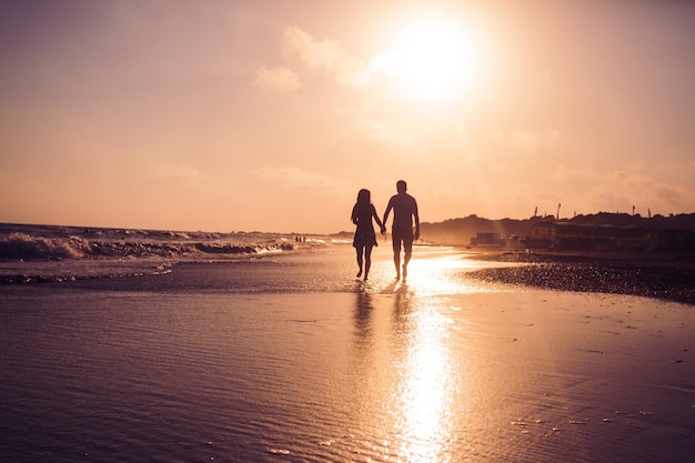 Silhueta de casal apaixonado que caminha ao longo de uma praia de areia e aprecia o pôr do sol