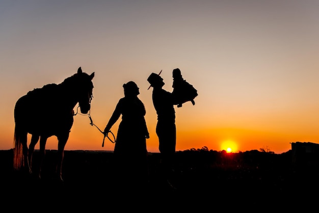 Foto silhueta de cavalo e família gaúcha ao pôr do sol na zona rural