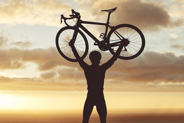 Silhueta de ciclismo e homem levantando uma bicicleta ao pôr do sol vitória torcendo e sucesso de objetivo esportivo bicicleta fitness e celebração do atleta na natureza após treinamento e realização de exercícios físicos