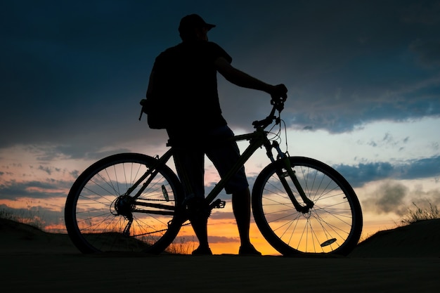 Silhueta de ciclista no fundo por do sol. Motociclista com bicicleta na areia durante o nascer do sol