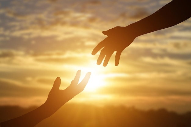 Silhueta de dar uma mão de ajuda, esperança e apoio uns aos outros sobre o fundo do pôr-do-sol