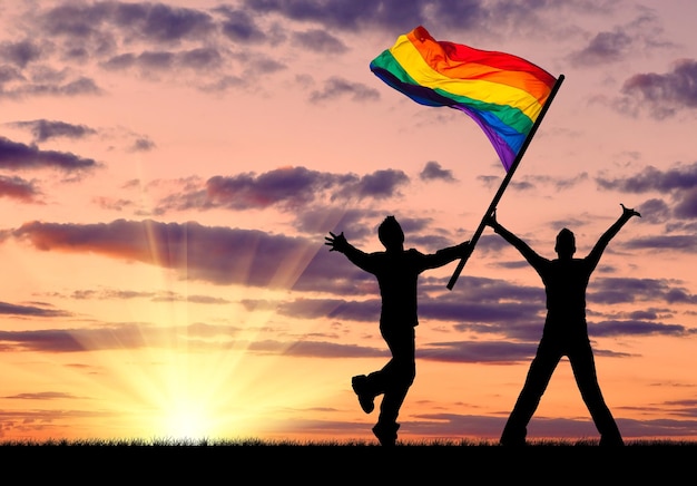 Silhueta de dois gays felizes na natureza e a bandeira do arco-íris na mão ao pôr do sol