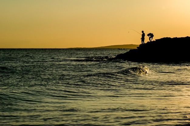 silhueta de dois pescadores em uma praia ao pôr do sol