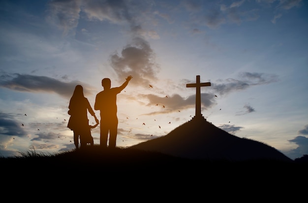 Silhueta de família cristã em pé com uma cruz para adorar a deus