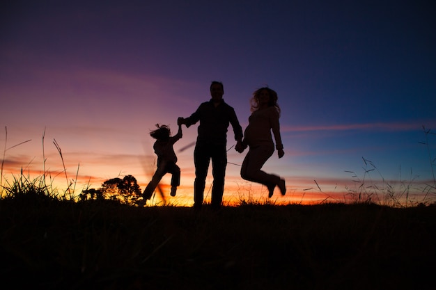 Silhueta de família feliz pulando no pôr do sol