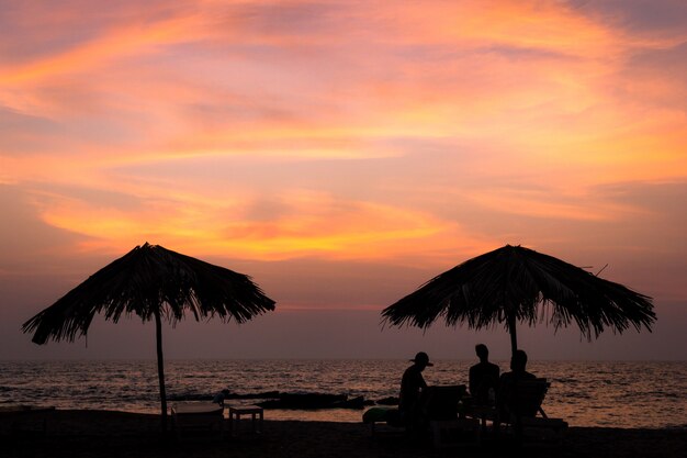 Silhueta de guarda-sóis e pessoas sentadas apreciando o pôr do sol dourado em Goa, Índia