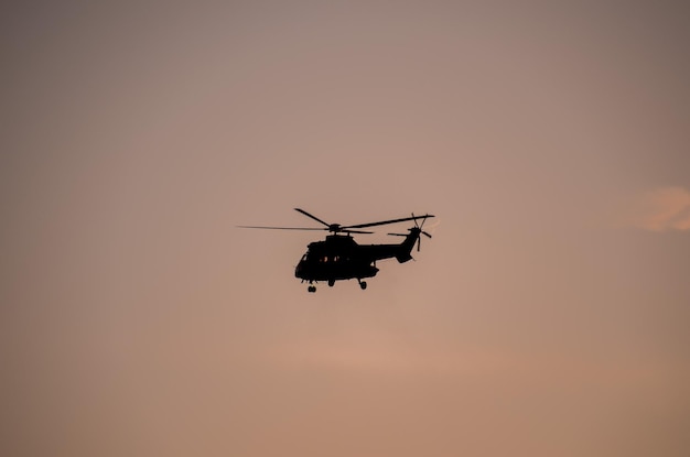 Silhueta de helicóptero militar voando sobre um céu escuro