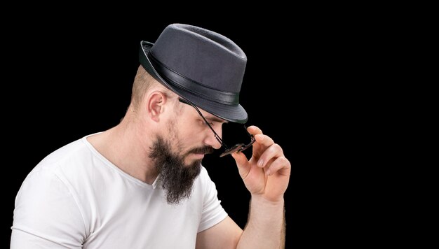 Silhueta de hipster confiante jovem barbudo bonito homem de chapéu e óculos de sol. estúdio, tiro na imagem de fundo escuro, com espaço de cópia gratuita