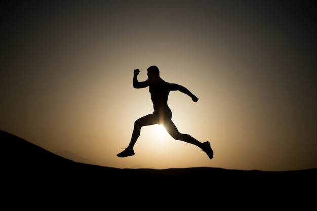 Foto silhueta de homem correndo no fundo do céu ardente do sol no futuro esporte de montanha e recreação