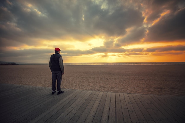 Silhueta de homem na praia olhando o pôr do sol dramático mágico