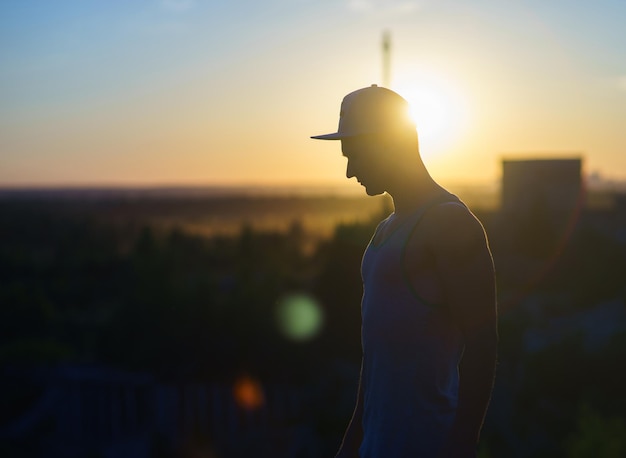 Silhueta de homem usando boné no fundo da paisagem urbana durante o pôr do sol