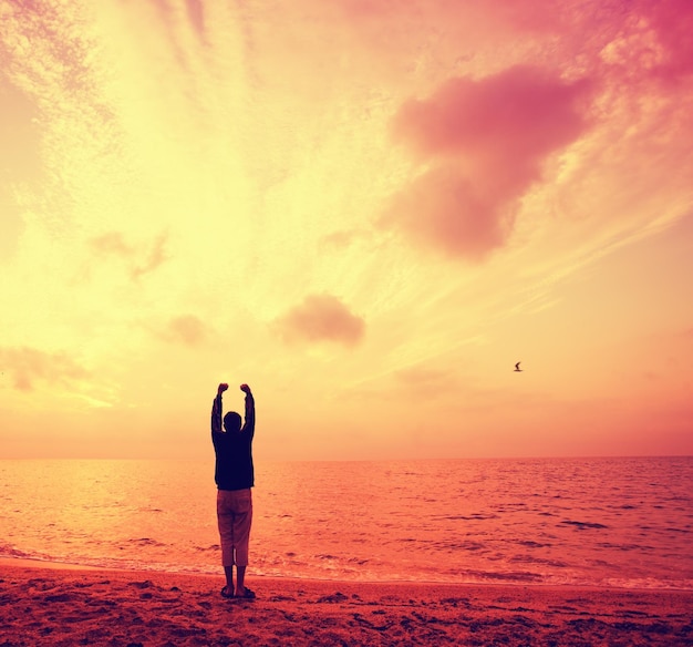 Silhueta de jovem com as mãos no ar na praia ao nascer do sol