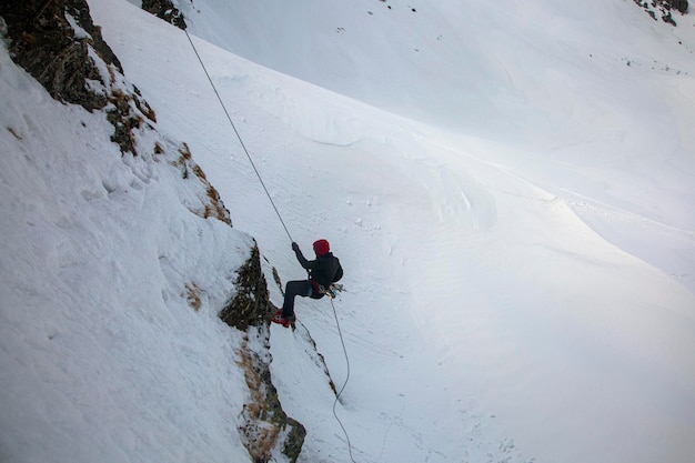 Silhueta de jovem descendo de um penhasco nevado Alpinista fazendo rapel de uma rocha branca