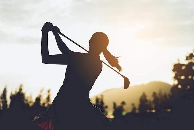 Silhueta de jovem jogador de golfe feminino varrer e manter o campo de golfe fazendo o balanço do golfe, ela se exercita para relaxar tempo, tom vintage