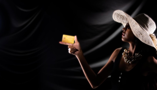 Silhueta de jovem segura cartão de crédito de ouro compra venda on-line sobre fundo preto de cortina de cortina