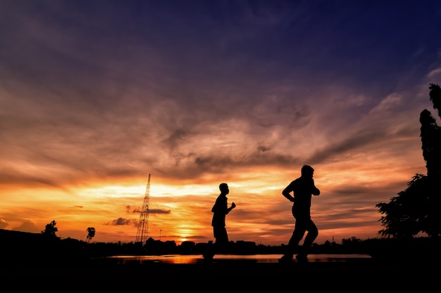 Silhueta de jovens a fazer jogging no parque ao pôr do sol.