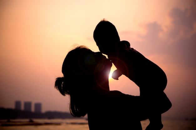 Silhueta de mãe brincando com seu bebê ao pôr do sol