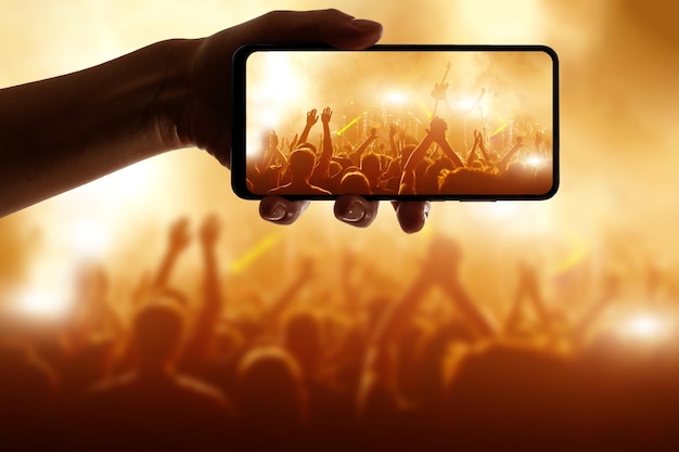 Silhueta de mão usando câmera do telefone para tirar fotos e vídeos no festival de concertos pop