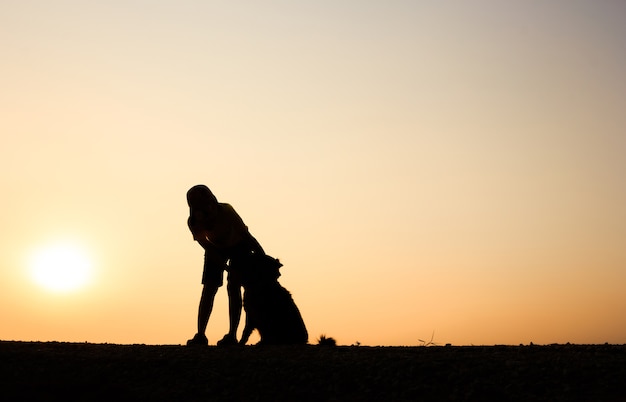 Silhueta de menina e seu cachorro com fundo bonito do por do sol.