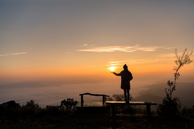 Silhueta de menina solitária em pé no topo da montanha com o nascer do sol