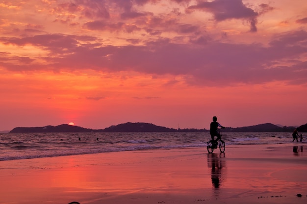 Silhueta de menino andar de bicicleta na praia com o céu do sol