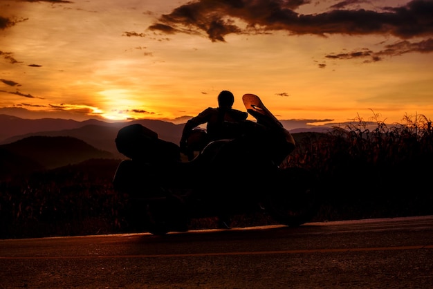 Foto silhueta de motociclista com estacionamento de motos de turismo no fundo da paisagem natural ao pôr do sol