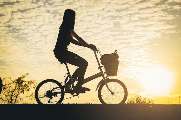 Foto silhueta de mulher andar de bicicleta ao longo da ciclovia no parque ao pôr do sol.