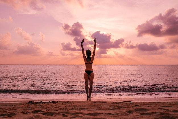 Silhueta de mulher com os braços erguidos contra a calma praia do sol. conceito de liberdade e sensação de bem-estar