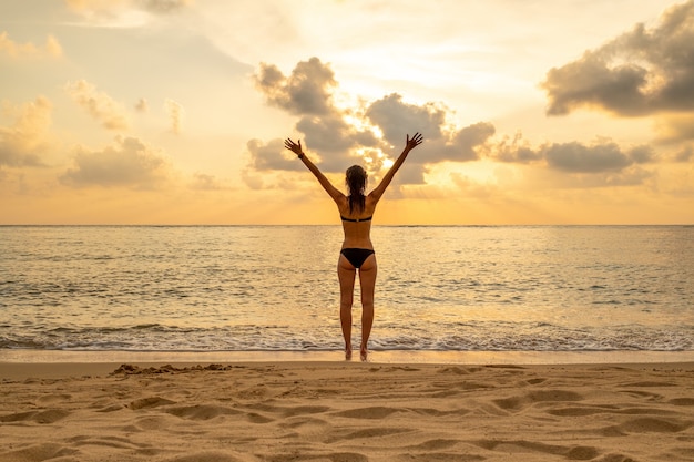 Silhueta de mulher com os braços erguidos contra a calma praia do sol. conceito de liberdade e sensação de bem-estar