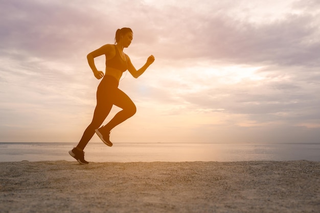 Silhueta de mulher corredor em execução de treinamento de treino na praia do sol. Silhueta de uma mulher atlética correndo na praia durante o tempo do sol.