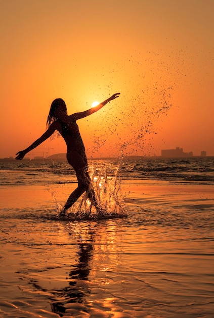 Silhueta de mulher dançando na água ao pôr do sol