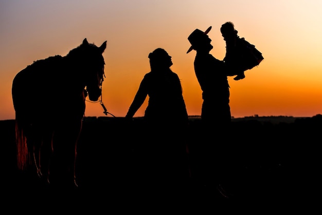 Silhueta de mulher de família de fazenda segurando cavalo e pai gaúcho segurando filha