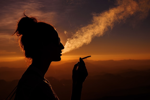 Foto silhueta de mulher fumando na paisagem do pôr do sol