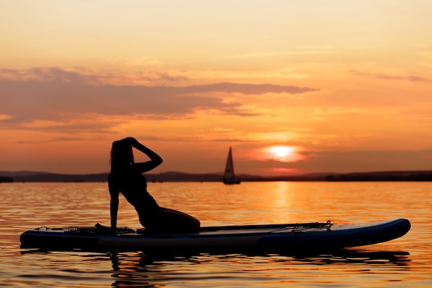 Silhueta de mulher garota paddle boarding ao pôr do sol