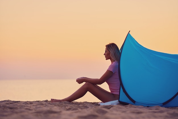 silhueta de mulher jovem em frente a uma tenda na praia ao nascer do sol