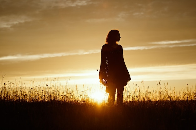 Silhueta de mulher jovem feliz no pôr do sol, garota ao ar livre em um poncho xadrez