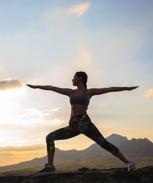 Silhueta de mulher jovem praticando ioga ou pilates no pôr do sol ou nascer do sol na localização da bela montanha.