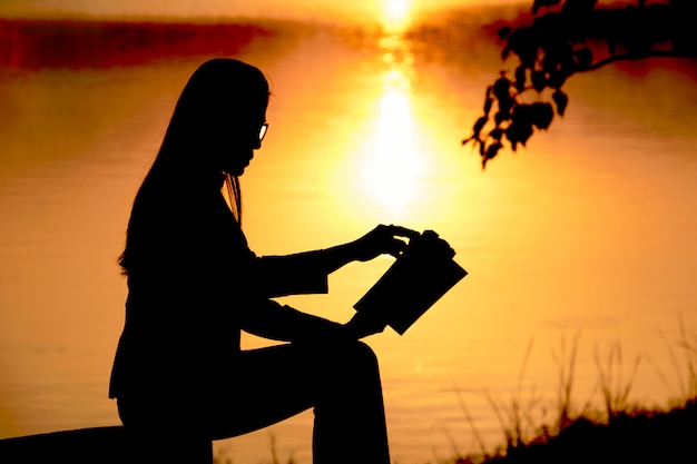 Silhueta de mulher ler um livro à beira do lago