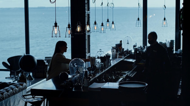 Silhueta de mulher pedindo coquetel com vista para o mar Garçom preparando bebidas
