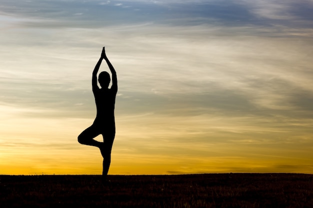 Silhueta de mulher praticando yoga no nascer do sol