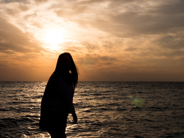 Silhueta de mulher vendo o sol na praia ao pôr do sol. turista de férias na praia