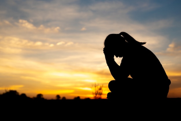 Silhueta de mulheres tristes e deprimidas sentadas na passarela do parque com o pôr do sol